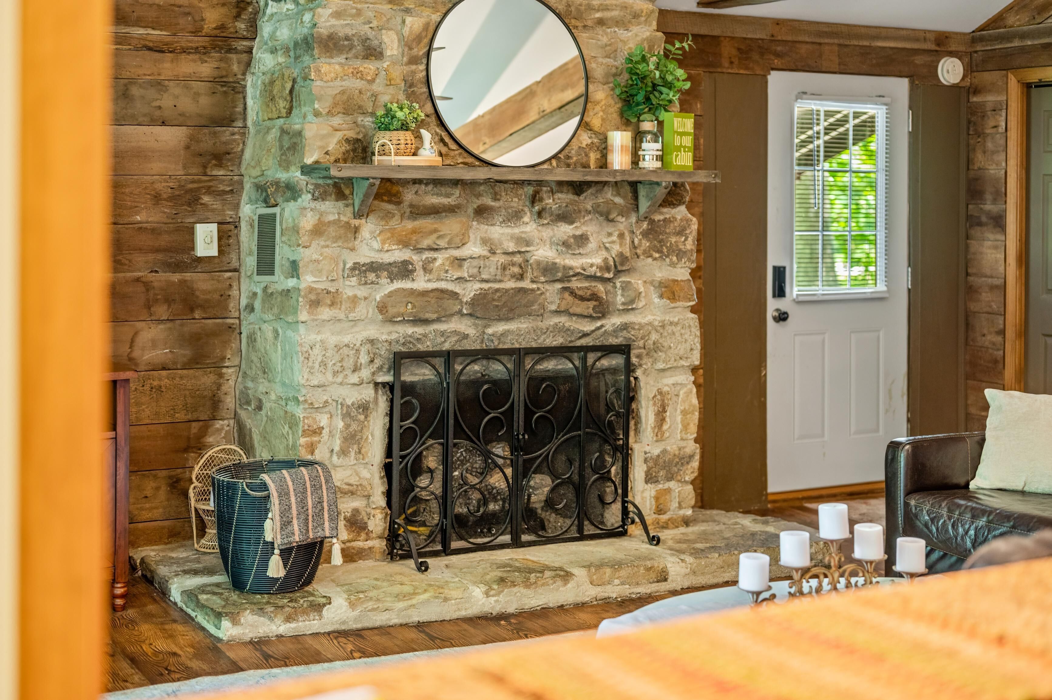 A rustic stone fireplace with a decorative metal grate, a wooden bench, and a door with a window.