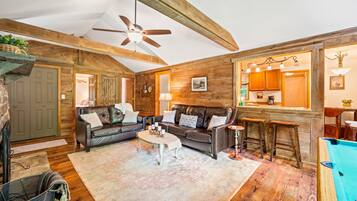 A cozy living room with a ceiling fan, wooden walls, a fireplace, a sofa, a coffee table, and a pool.