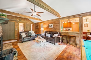 A cozy living room with a ceiling fan, wooden walls, a fireplace, a sofa, a coffee table, and a pool.