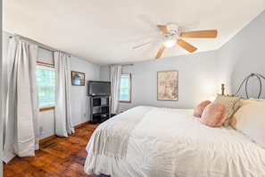 A bedroom with a bed, a ceiling fan, a TV, and a window with curtains.