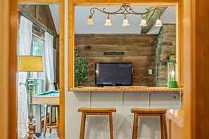 Una habitación con un espejo de marco de madera, un televisor y dos taburetes de madera.