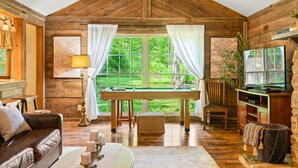Una stanza accogliente con soffitto in legno, tavolo da biliardo, televisione e un'area salotto confortevole.