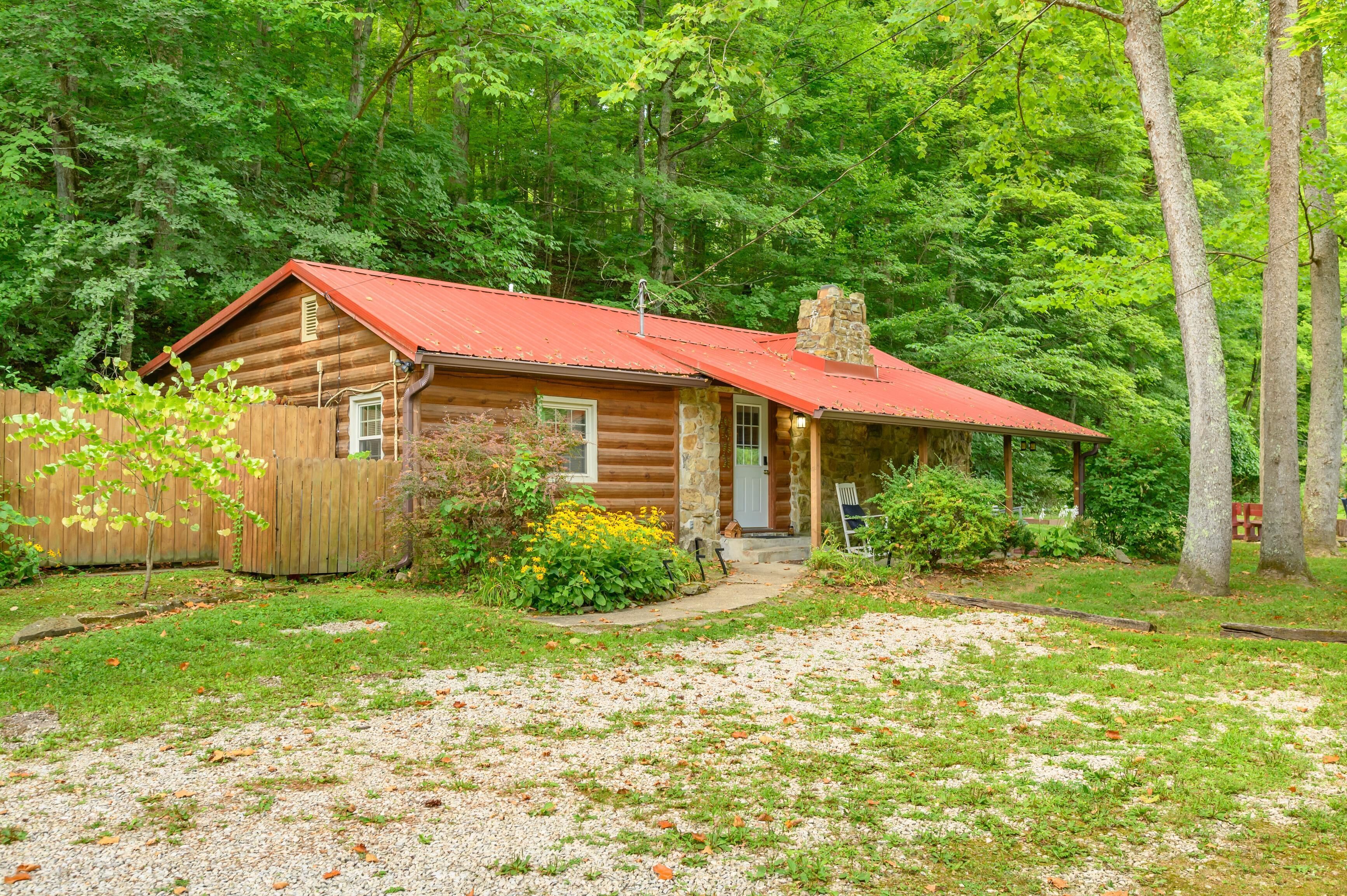 A rustic cabin with a red roof, surrounded by dense green foliage.