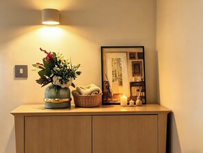 Ein Holzschrank mit einer Blumenvase, einer Kerze und einem gerahmten Bild an der Wand.
