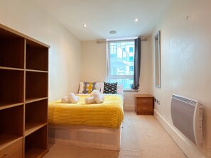 Ein Schlafzimmer mit Bett, einem Fenster mit Vorhängen, einer Heizung und einem Holzschrank.