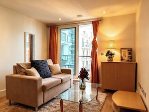 Ein modernes Wohnzimmer mit einer Couch, einem Glastisch, einer Holzkabine und Blick auf die Stadt durch große Fenster.