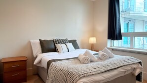 A hotel room with a bed, a nightstand, a lamp, and a window with curtains. - Cosy 2BRs Apt w/AC and balcony near Vauxhall (London)