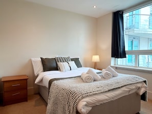 A hotel room with a bed, a nightstand, a lamp, and a window with curtains. - Cosy 2BRs Apt w/AC and balcony near Vauxhall (London)