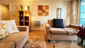 A modern living room with two sofas, a coffee table, a rug, a wall-mounted air conditioner, and a painting. - Cosy 2BRs Apt w/AC and balcony near Vauxhall (London)