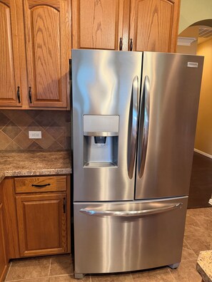 A stainless steel refrigerator with a water dispenser, wooden cabinets, and a granite countertop. - Welcoming 4BR Luxury house with private POOL in charming Forney (Forney)