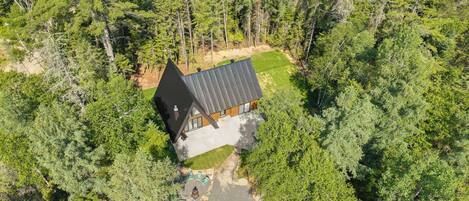 A modern house with a sloped roof, surrounded by dense forest.