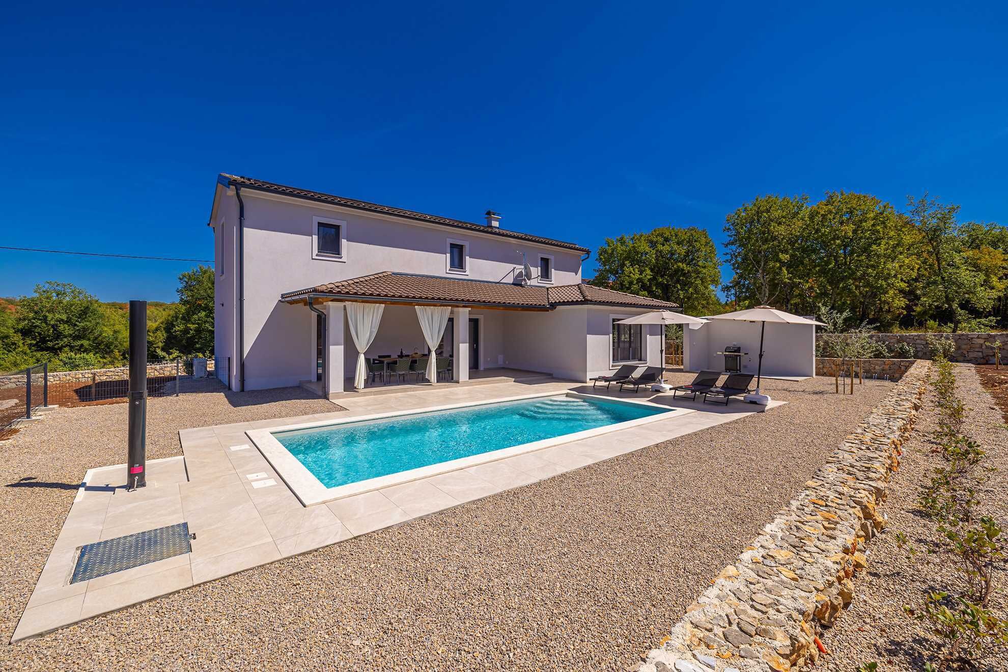 A two-story house with a swimming pool, outdoor seating, and a stone wall.