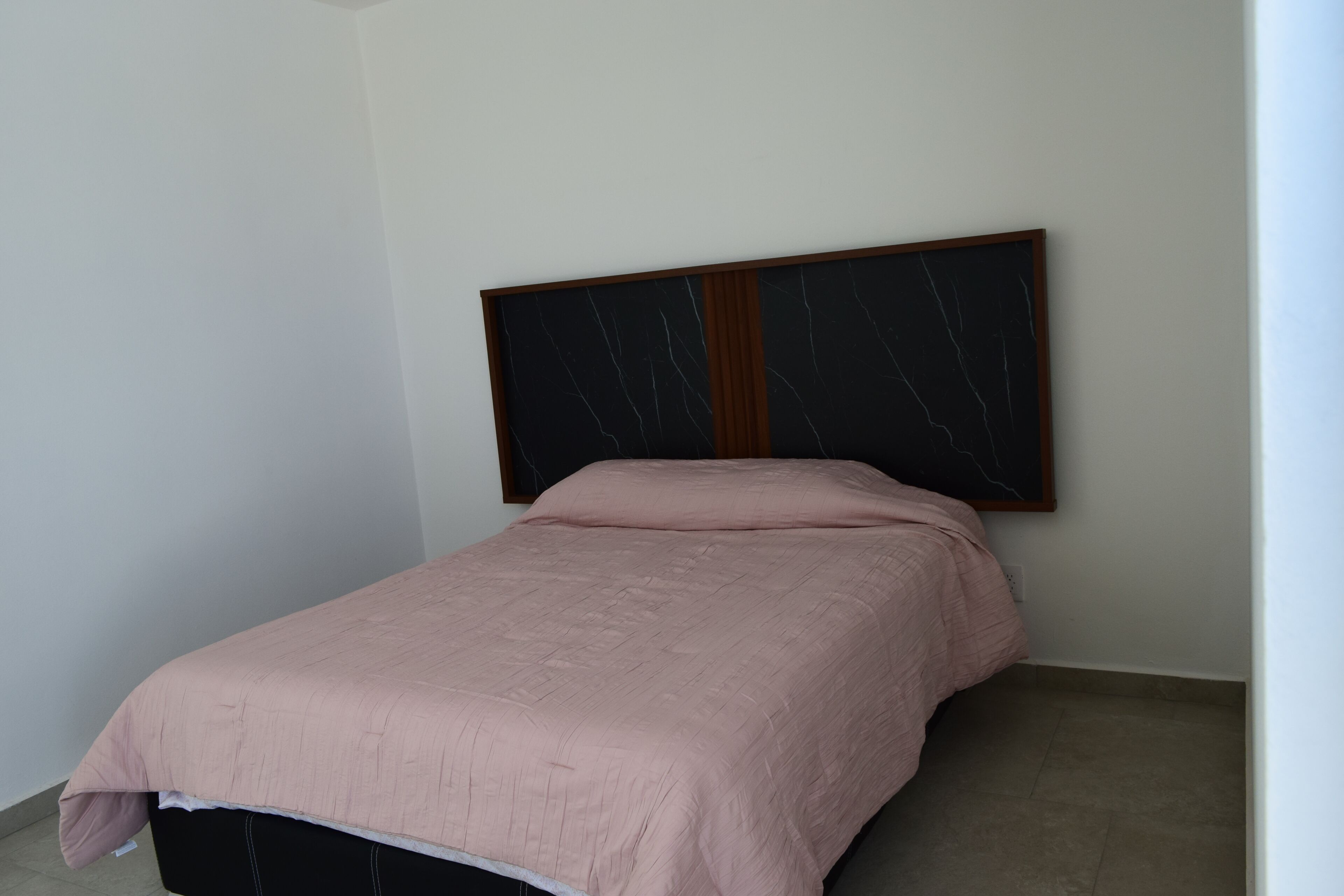 A single bed with a headboard against a plain wall, a small bedside table, and a light-colored floor.