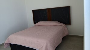 A single bed with a headboard against a plain wall, a small bedside table, and a light-colored floor.
