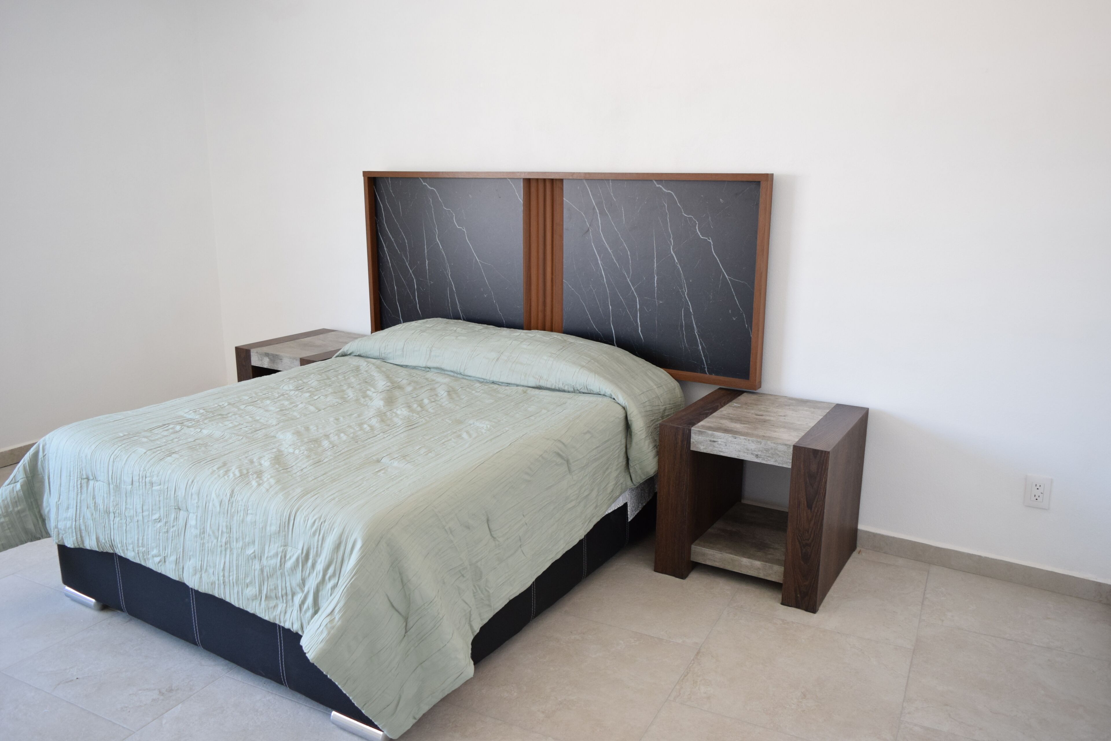 A bed with a headboard, two bedside tables, and a light-colored floor.