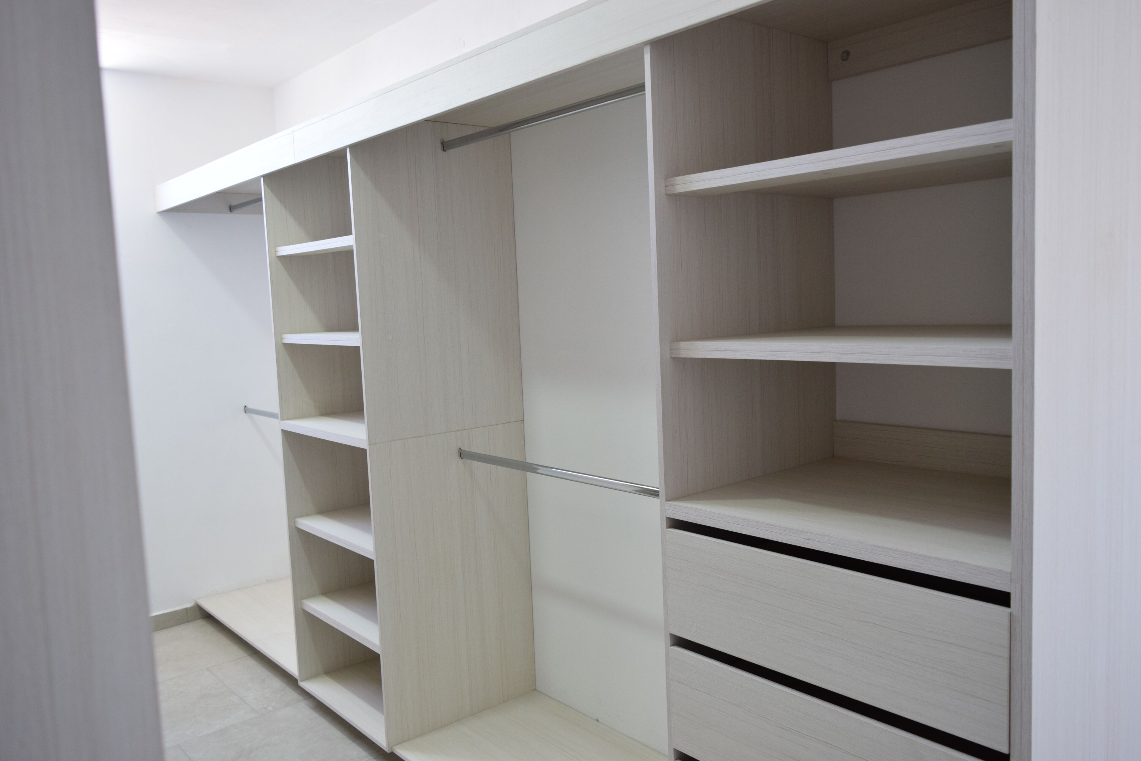 A walk-in closet with multiple shelves and drawers, featuring a light wood finish and metal handles.