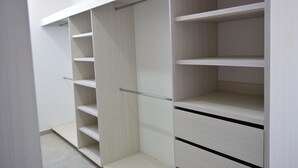 A walk-in closet with multiple shelves and drawers, featuring a light wood finish and metal handles.