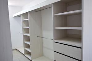 A walk-in closet with multiple shelves and drawers, featuring a light wood finish and metal handles.