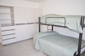 A bunk bed with a green mattress, a white wardrobe with multiple shelves, and a tiled floor.