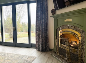 Una habitación con chimenea, un ventanal con cortinas y vistas al exterior.
