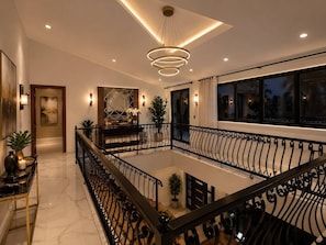 Een ruime binnenruimte met een open centrale zone, een balkon met een hekwerk en een moderne kroonluchter.