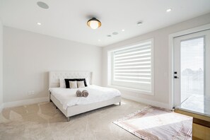 A bedroom with a bed, a large window with blinds, a ceiling light, and a door. - Whiterock holiday heaven (Surrey)