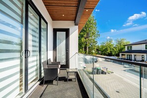 Ein Balkon mit Glasgeländer, einer Tür und einer Sitzecke mit Stühlen und einem Tisch.