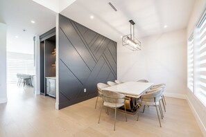 A modern dining area with a white table and chairs, a geometric wall design, and a pendant light. - Whiterock holiday heaven (Surrey)