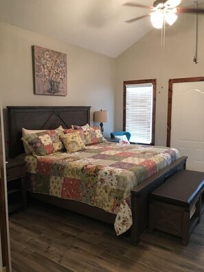 A bedroom with a bed, a nightstand, a bench, a ceiling fan, a window with blinds, and a door.
