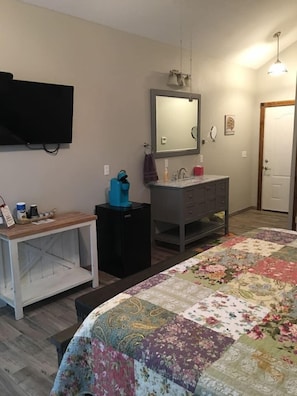A bedroom with a bed, a dresser, a mirror, a television, and a small table. - Prairie Cottage King Suite 1/2 block from PW Merc (Pawhuska)
