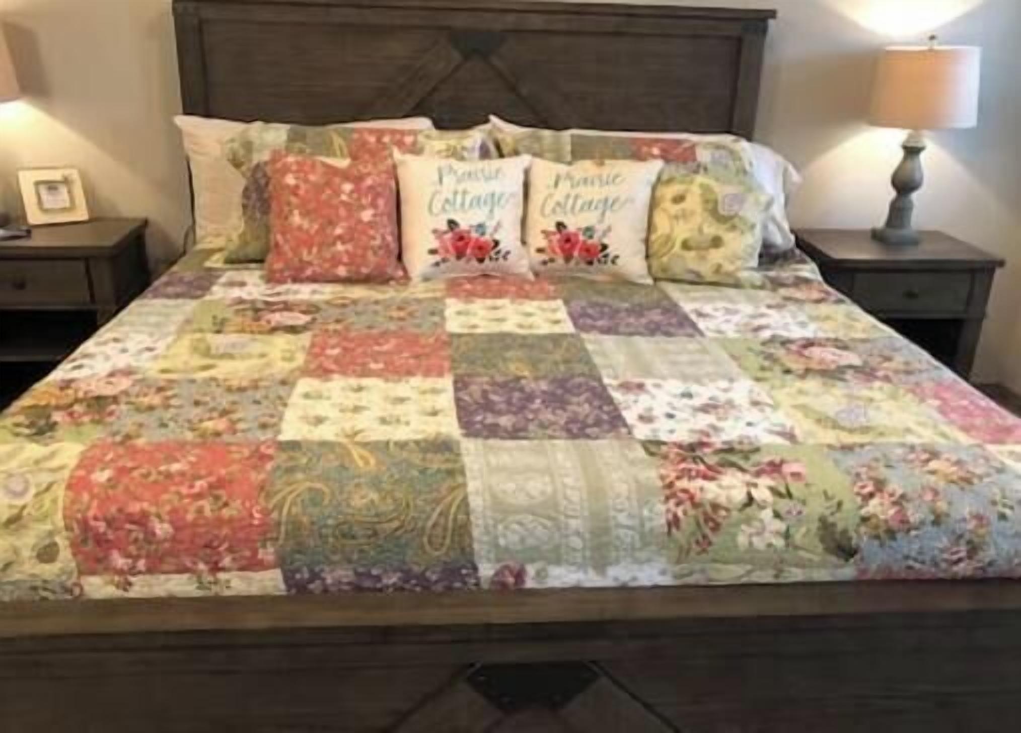 A bed with a quilt, pillows, and a bedside lamp.