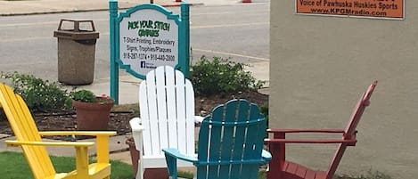Outdoor seating with Adirondack chairs and a sign for a business offering T-shirt printing and embroidery.