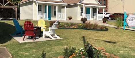 Una cabaña de dos pisos con un porche, un césped con sillas Adirondack de colores y un parterre de flores.