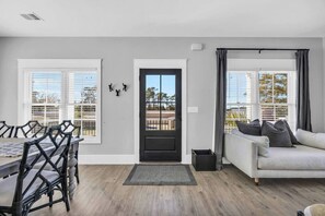 A modern living room with a dining area, a black door, and large windows with blinds. - HoT TuB PooL Sauna 5 BeD Pet Friendly Mansion (Murrells Inlet)