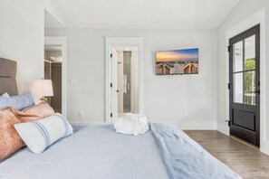 A bedroom with a bed, a nightstand, a lamp, a painting, and a door leading to another room. - HoT TuB PooL Sauna 5 BeD Pet Friendly Mansion (Murrells Inlet)