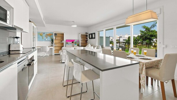 Una cocina moderna con una isla central, taburetes de bar y un comedor con vistas.