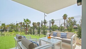 Un patio con una mesa blanca, un sofá beige y una barandilla de cristal.