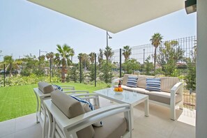 A patio with a white table, beige sofa, and a glass balustrade. - Corner property-free parking-Pool-close to beach - Acgua Garden B-1-BA (Marbella)