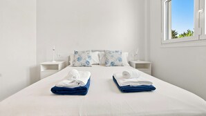 Habitación de hotel con una cama grande, dos mesitas de noche, un ventanal con vistas a la vegetación y una pared blanca.