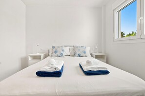 A hotel room with a large bed, two nightstands, a window with a view of greenery, and a white wall. - Corner property-free parking-Pool-close to beach - Acgua Garden B-1-BA (Marbella)