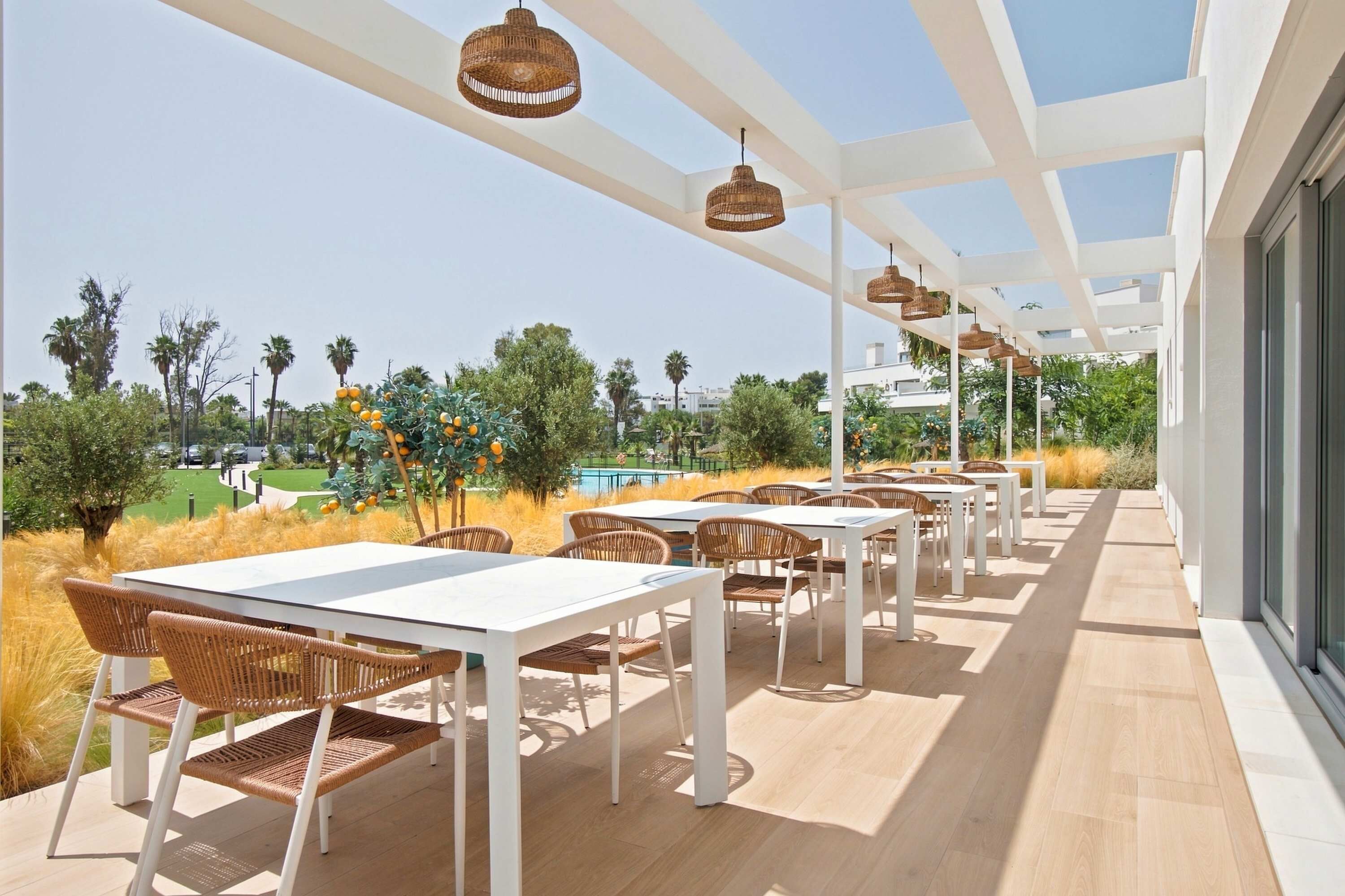 An outdoor patio area with white tables and wicker chairs, a clear sky, and a view of a golf course.