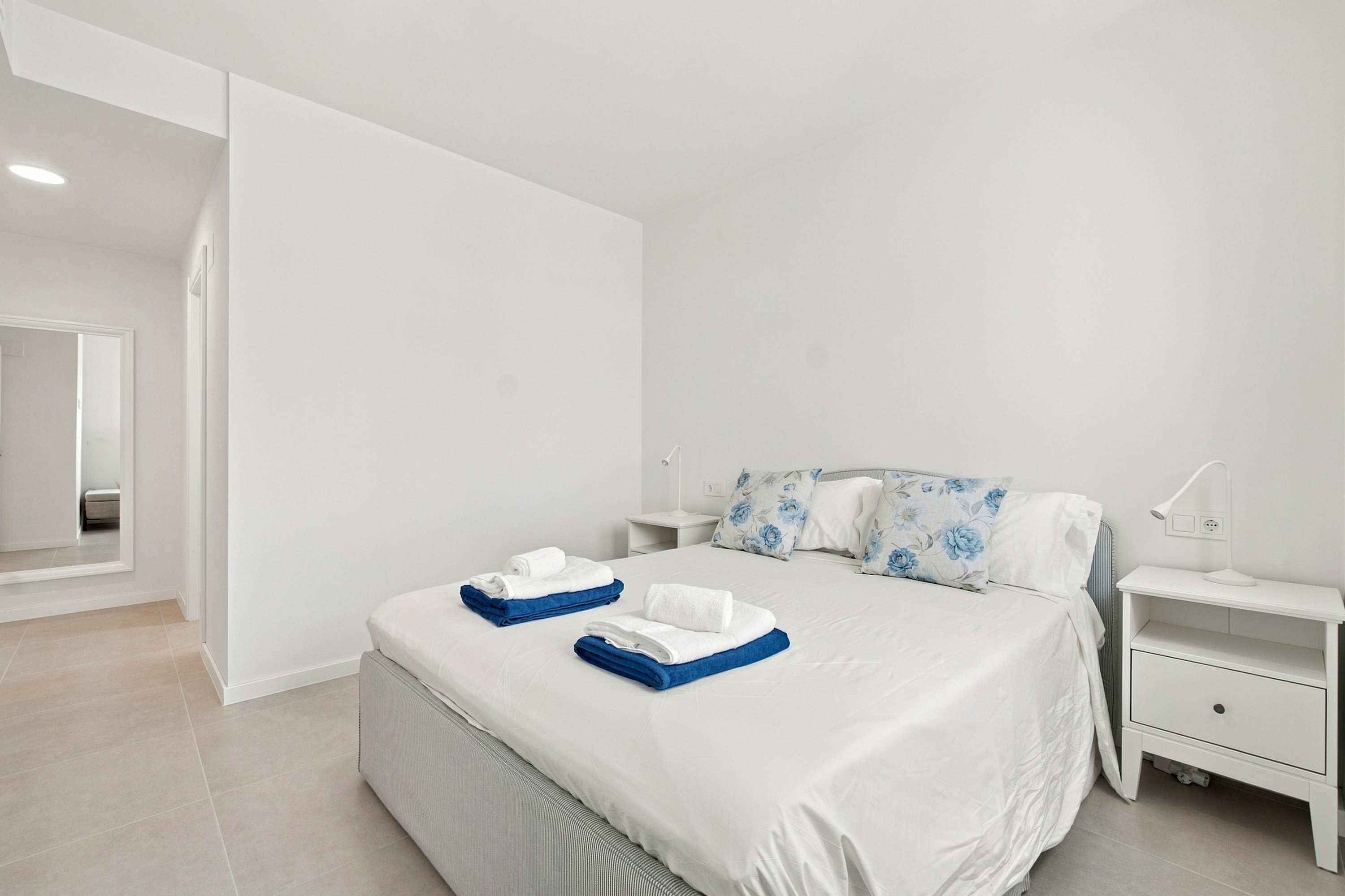 A hotel room with a bed, a nightstand, a mirror, and a bedside table with a lamp.