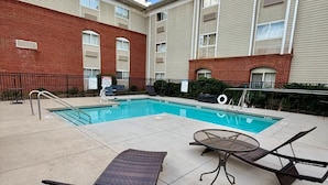 A swimming pool with lounge chairs and a table, surrounded by a brick building with multiple windows.
