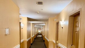 A hotel corridor with doors on both sides, a carpeted floor, and light fixtures on the walls.