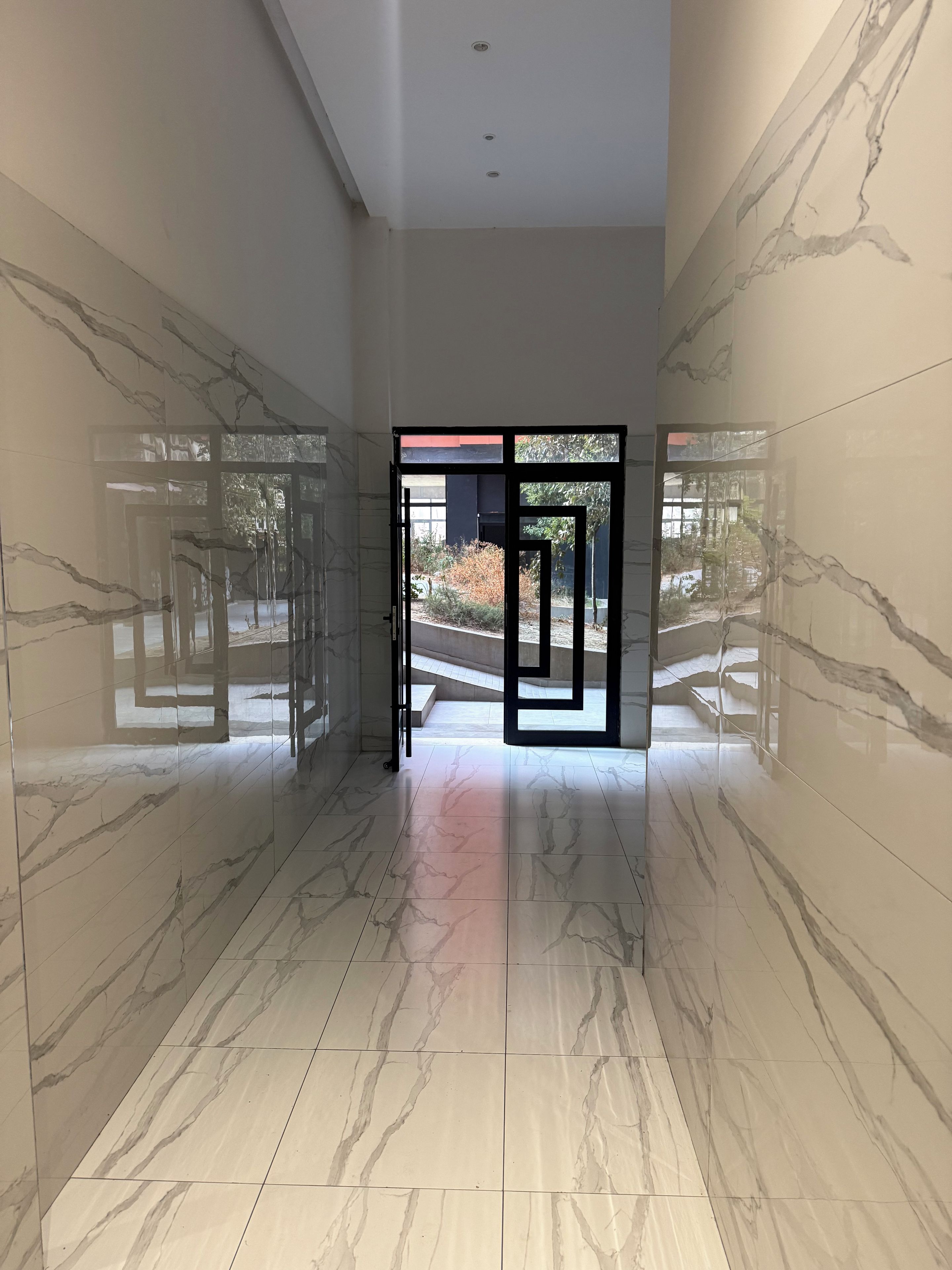 A corridor with marble flooring and walls, leading to an open area with a view of the outdoors.