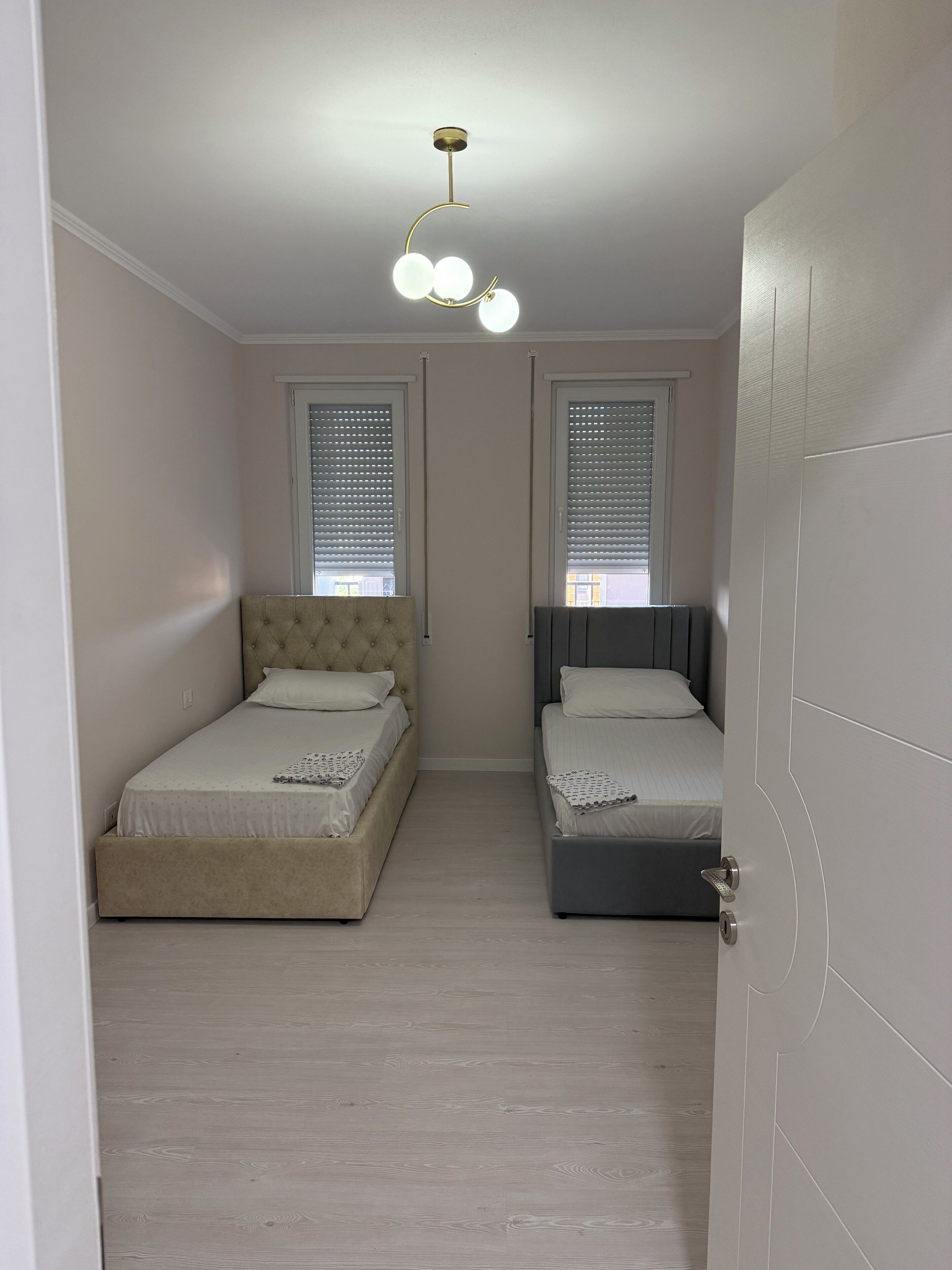 A bedroom with two beds, a ceiling light fixture, and a door.