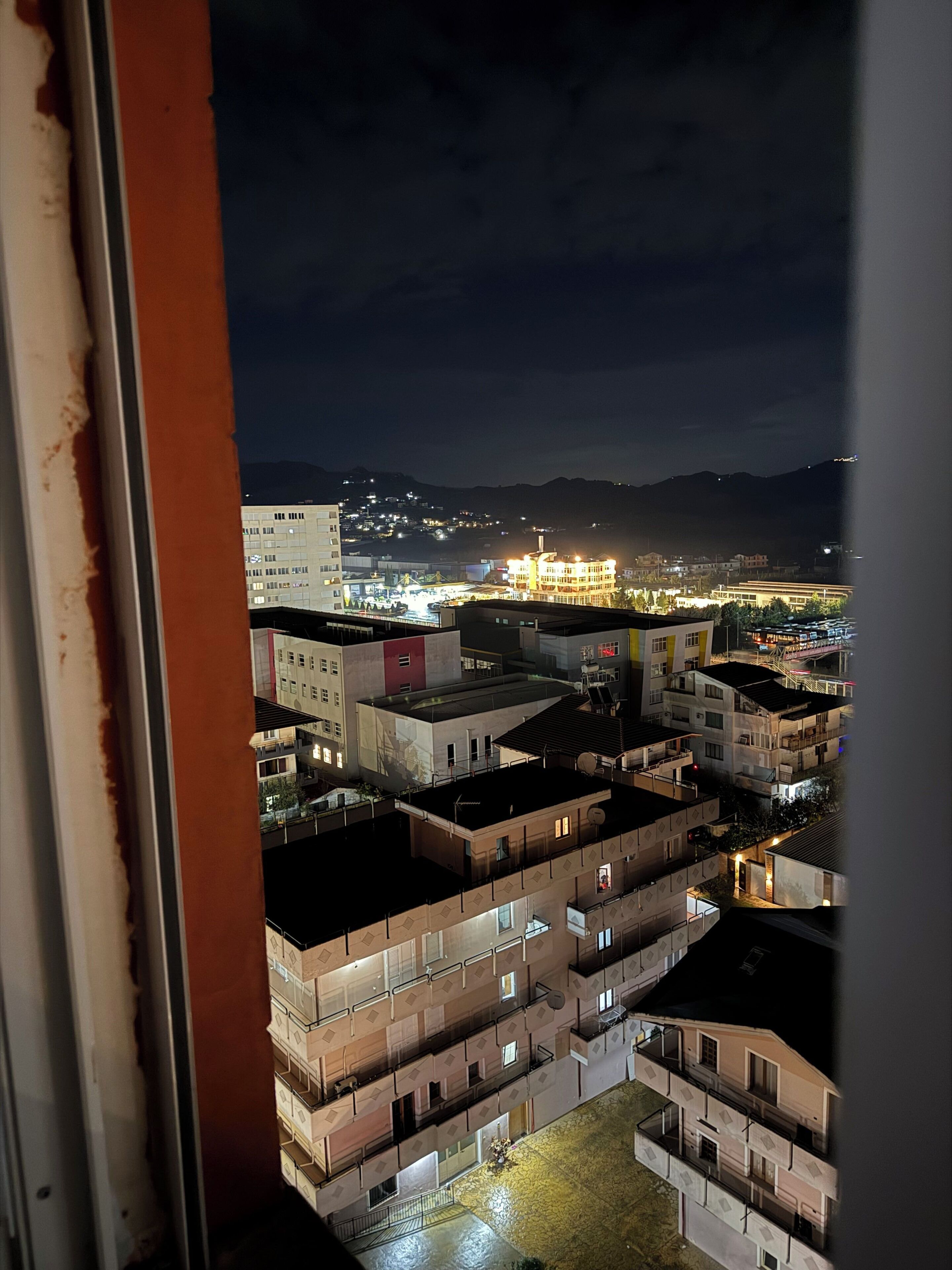 Una vista notturna di un paesaggio urbano con edifici e una montagna sullo sfondo.