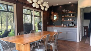 A modern kitchen with a wooden dining table and metal chairs, a built-in oven, and a large window overlooking greenery. - Blissful Marsh Front GuestHouse Getaway! (Charleston)