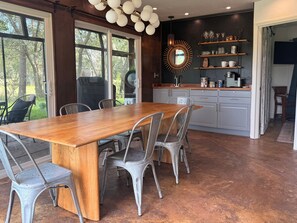 A modern kitchen with a wooden dining table and metal chairs, a built-in oven, and a large window overlooking greenery. - Blissful Marsh Front GuestHouse Getaway! (Charleston)