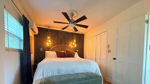 A bedroom with a bed, a ceiling fan, a window with blinds, a door, and a patterned rug. - Blissful Marsh Front GuestHouse Getaway! (Charleston)